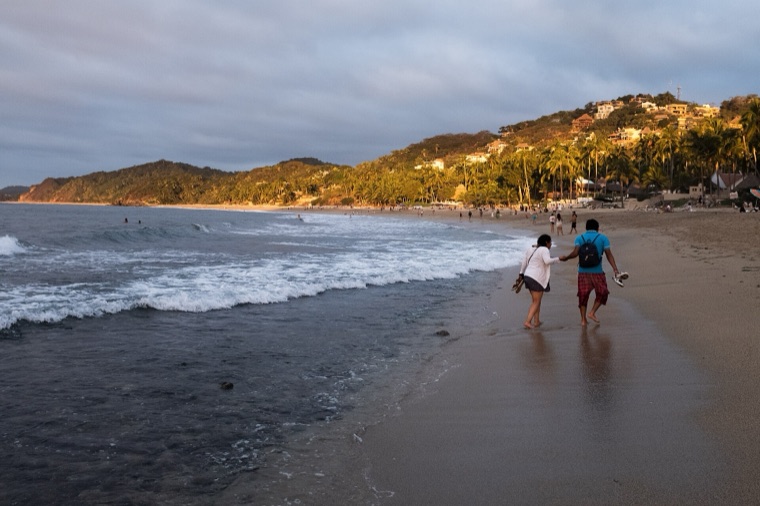 A couple strolling a Riviera Nayarit beach with the town on the hillside